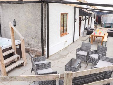 An outdoor patio area with wicker chairs and table a wooden dining table with benches and colorful cups and a hot tub at Maestyddyn Farm House in Clawddnewydd near Ruthin