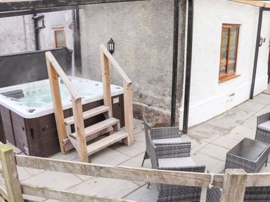 An outdoor patio with a hot tub and wooden steps and wicker chairs with a table at Maestyddyn Farm House in Clawddnewydd near Ruthin