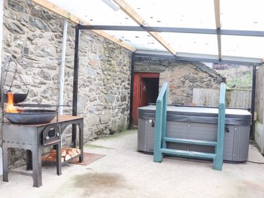 An outdoor covered patio area with a stone wall fire pit and a hot tub with green steps at Maestyddyn Farm House Clawddnewydd near Ruthin