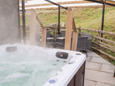An outdoor covered patio with a hot tub and wicker chairs around a table at Maestyddyn Farm House in Clawddnewydd near Ruthin