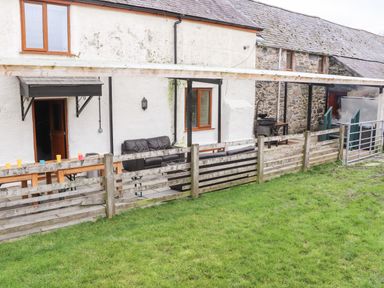 An outside seating area with a wooden fence and tables in front of a farmhouse at Maestyddyn Farm House in Clawddnewydd near Ruthin