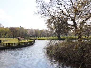 A park with a pond benches and trees with a wooden fence along the water at Maestyddyn Farm House Clawddnewydd near Ruthin