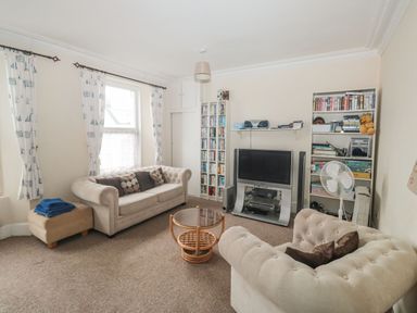 A living room with two beige sofas a round glass coffee table a television and bookshelves at Dunholme House in Teignmouth