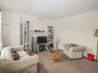 A living room with two beige sofas a glass top coffee table a television with bookshelves and a standing fan at Dunholme House in Teignmouth