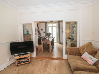 A living room with a brown sofa and a television on a wooden stand looking into a dining room with a wooden table and chairs at Dunholme House in Teignmouth