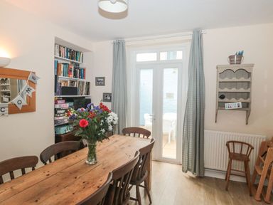 A dining room with a wooden table and chairs a vase with flowers a bookshelf and glass doors with curtains at Dunholme House in Teignmouth
