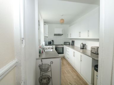 A narrow kitchen with white cabinets and countertop appliances at Dunholme House in Teignmouth