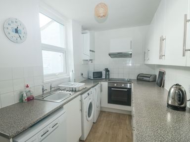 A kitchen with white cabinets grey countertops a sink washing machine microwave oven and kettle at Dunholme House in Teignmouth