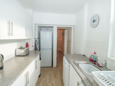 A kitchen with a fridge four slice toaster kettle dishwasher sink and wall clock at Dunholme House in Teignmouth