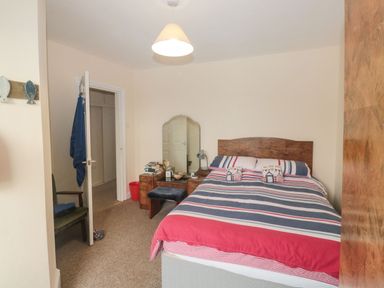 A bedroom with a bed with striped bedding and a wooden headboard a dressing table with a mirror books and a stool a chair and an open door at Dunholme House in Teignmouth