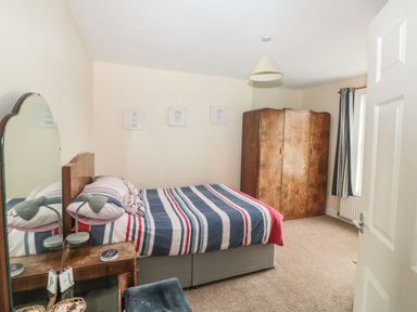A bedroom with a bed with striped bedding a wooden wardrobe a vanity table with a mirror and a lamp at Dunholme House in Teignmouth