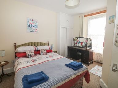 A bedroom with a bed with seaside themed bedding a wooden dressing table with a mirror and chair at Dunholme House in Teignmouth