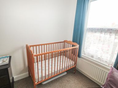 A wooden baby crib next to a window with blue curtains and a white radiator below at Dunholme House in Teignmouth
