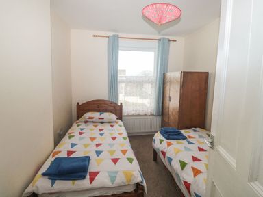 A bedroom with two single beds a wooden wardrobe and a window with curtains at Dunholme House Teignmouth