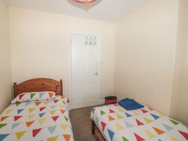 A bedroom with two single beds with colorful triangular patterned bedding a white door and a small red stool at Dunholme House in Teignmouth