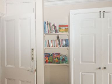 A small built-in bookshelf with books and children's books between a door and a double closet door in a room at Dunholme House in Teignmouth