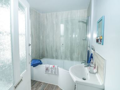A bathroom with a bathtub and glass shower screen a sink with a faucet and a blue towel hanging on the wall at Dunholme House in Teignmouth