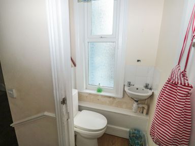 A small bathroom with a toilet, a corner sink, a window with frosted glass, and a red and white striped bag hanging on the wall at Dunholme House in Teignmouth