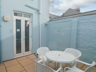 An outdoor patio area with a round white plastic table and four white plastic chairs near a pale blue door and walls with a clothesline above Dunholme House in Teignmouth