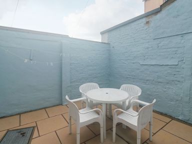 An outdoor patio area with a round white plastic table and four white plastic chairs with blue brick walls at Dunholme House in Teignmouth