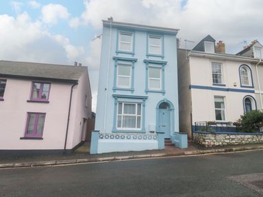 A street view of three attached houses with different pastel colors and windows in Teignmouth