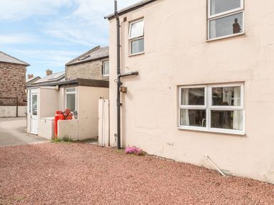 Exterior of a beige building with windows and two red gas cylinders near a small extension at Fisherman's Cottage in Seahouses