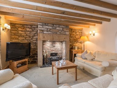 A living room with wooden beams a stone fireplace sofas a TV on a wooden stand and a wooden coffee table with cups at Fisherman's Cottage in Seahouses