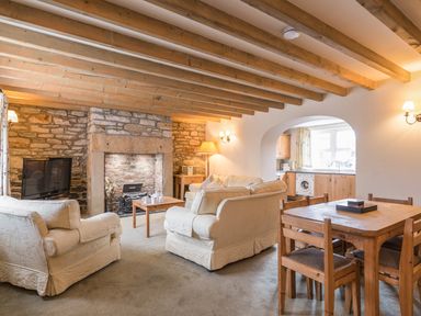A living room with armchairs a sofa a wooden dining table and chairs a fireplace and a view into a kitchen at Fisherman's Cottage in Seahouses