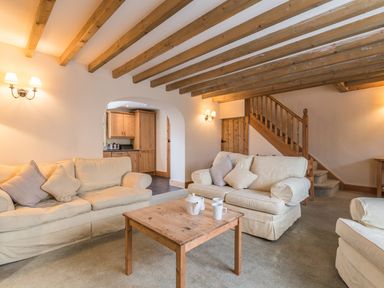 A living room with beige sofas a wooden coffee table and exposed wooden ceiling beams at Fisherman's Cottage in Seahouses