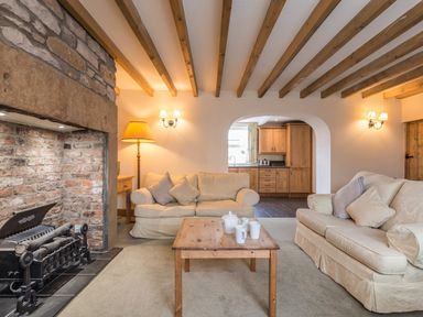 A living room with two sofas a wooden coffee table a stone fireplace and a view into a kitchen at Fisherman's Cottage in Seahouses