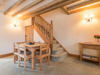 A dining area with wooden table and chairs next to carpeted stairs and wooden side table with flowers at Fisherman's Cottage in Seahouses