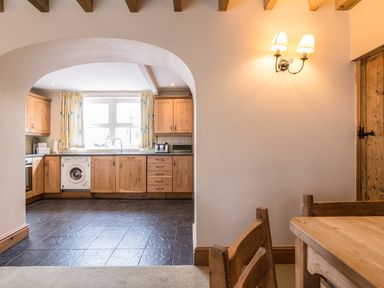 A kitchen with wooden cabinets a washing machine and a dining area with wooden table and chairs at Fisherman's Cottage in Seahouses