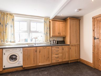 A kitchen with wooden cabinets a washing machine and a window with curtains at Fisherman's Cottage in Seahouses