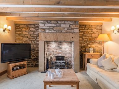 A living room with a stone fireplace a TV on a wooden stand a wooden coffee table with a tea set and a sofa with cushions at Fisherman's Cottage in Seahouses