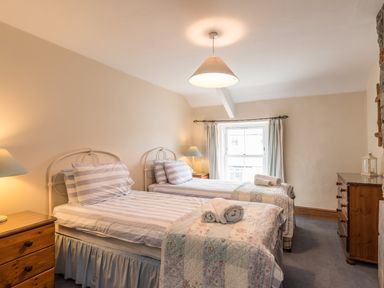 A bedroom with two single beds side by side with striped bedding and folded towels on top and wooden furniture at Fisherman's Cottage in Seahouses