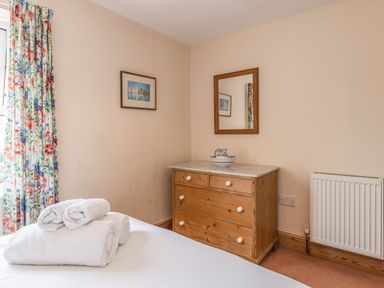 A bedroom corner with a wooden chest of drawers a mirror above and folded white towels on a bed at Fisherman's Cottage in Seahouses