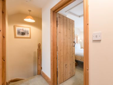 A hallway with stairs and a wooden door leading to a bedroom with a bed and bedside lamp at Fisherman's Cottage in Seahouses
