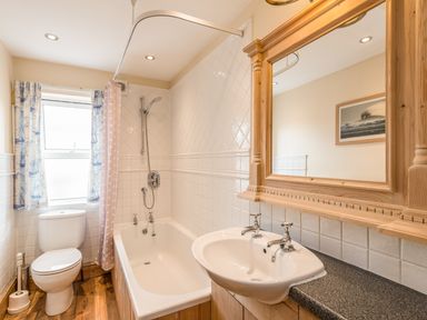 A bathroom with a toilet sink bathtub shower and wooden framed mirror at Fisherman's Cottage in Seahouses