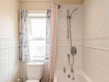 A bathroom with a toilet near a window and a bathtub with a showerhead at Fisherman's Cottage in Seahouses