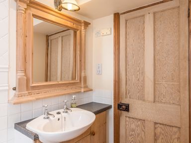 A bathroom sink with taps mirror above and wooden door at Fisherman's Cottage in Seahouses
