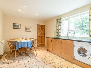 A kitchen with wooden cabinets a dining table set with breakfast near a window at Brians Cottage in Alnmouth