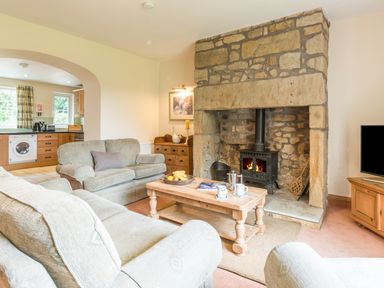 A living room with stone fireplace sofas wooden coffee table and kitchen visible through archway at Brians Cottage in Alnmouth