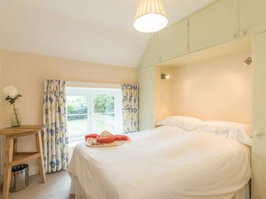 A bedroom with a bed, bedside lights, a small wooden table with a vase, and a window with floral curtains at Brian's Cottage in Alnmouth