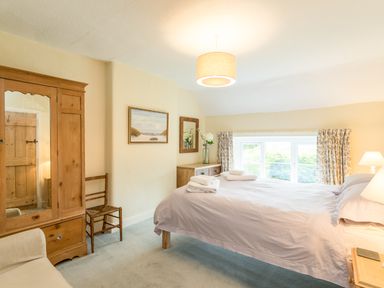 A bedroom with a double bed window wooden wardrobe and chair at Brians Cottage in Alnmouth