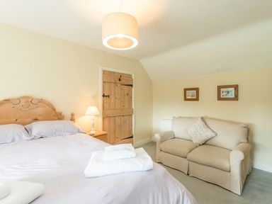 A bedroom with a bed, bedside table with lamp, wooden door, beige sofa, and two framed pictures on the wall at Brians Cottage in Alnmouth