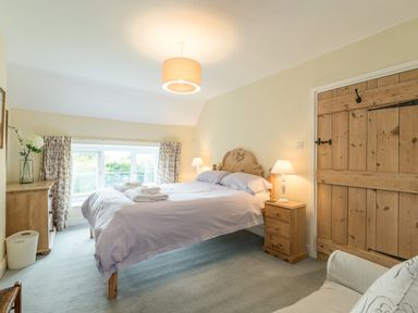 A bedroom with a double bed bedside tables lamps a wooden chest of drawers a wooden door and a window with floral curtains at Brians Cottage in Alnmouth