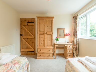 A bedroom with two beds bedside desk wardrobe wooden door and window at Brians Cottage in Alnmouth