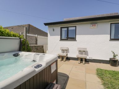 An outdoor patio area with a hot tub wooden chairs and a white building at Minerva in Trearddur Bay