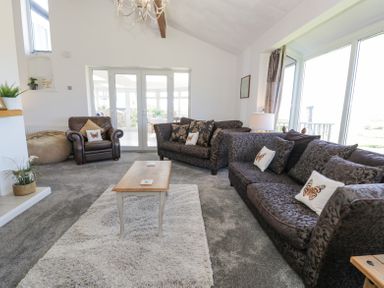 A living room with two patterned sofas a leather armchair a wooden coffee table and large windows at Minerva in Trearddur Bay