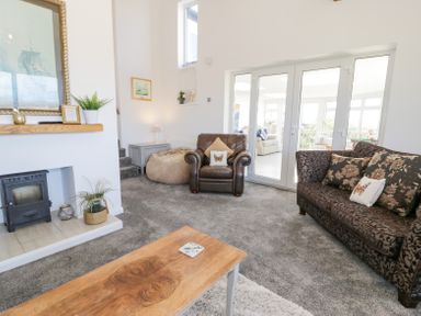 A living room with a wood burning stove armchair sofa coffee table and glass doors leading to another room at Minerva in Trearddur Bay
